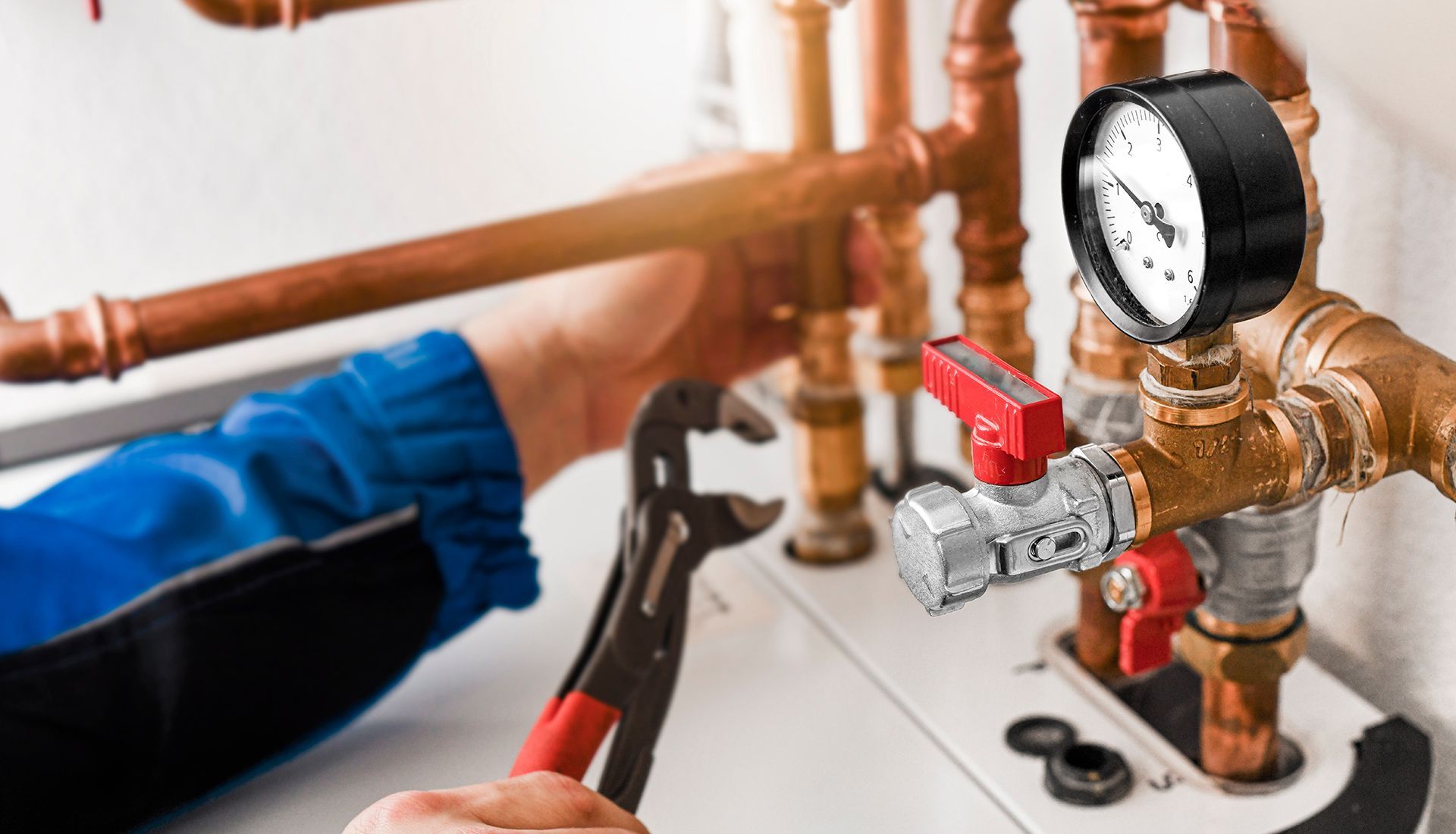 Plumber working on copper pipes with a wrench; a pressure gauge is visible.
