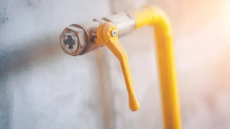 Hand turning a red valve on a water heater, close-up view.