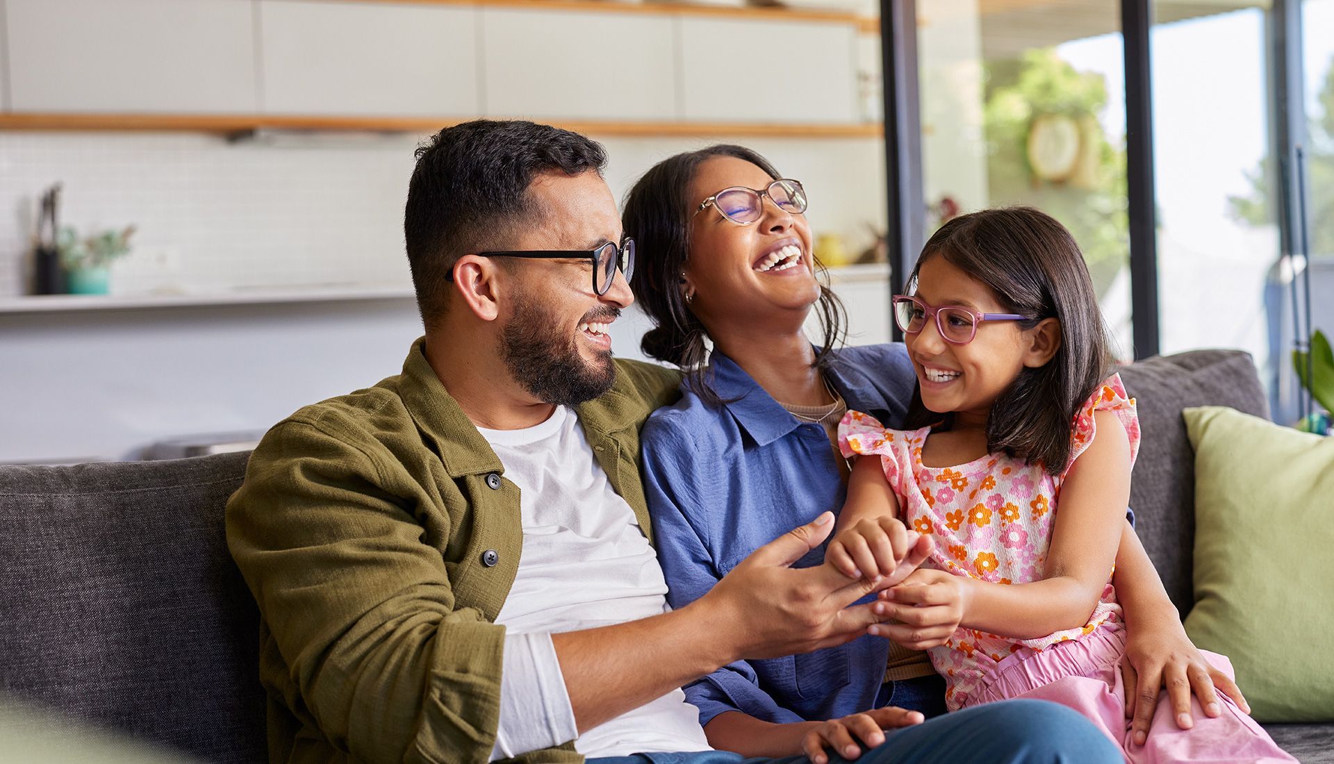 Family of three laughing together on a couch in a living room.