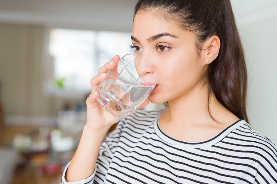 Woman drinking from a glass of water, inside a home.