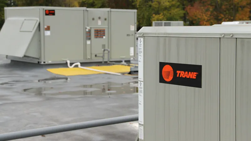 Rooftop with several industrial HVAC units, one with a Trane logo on a grey building.
