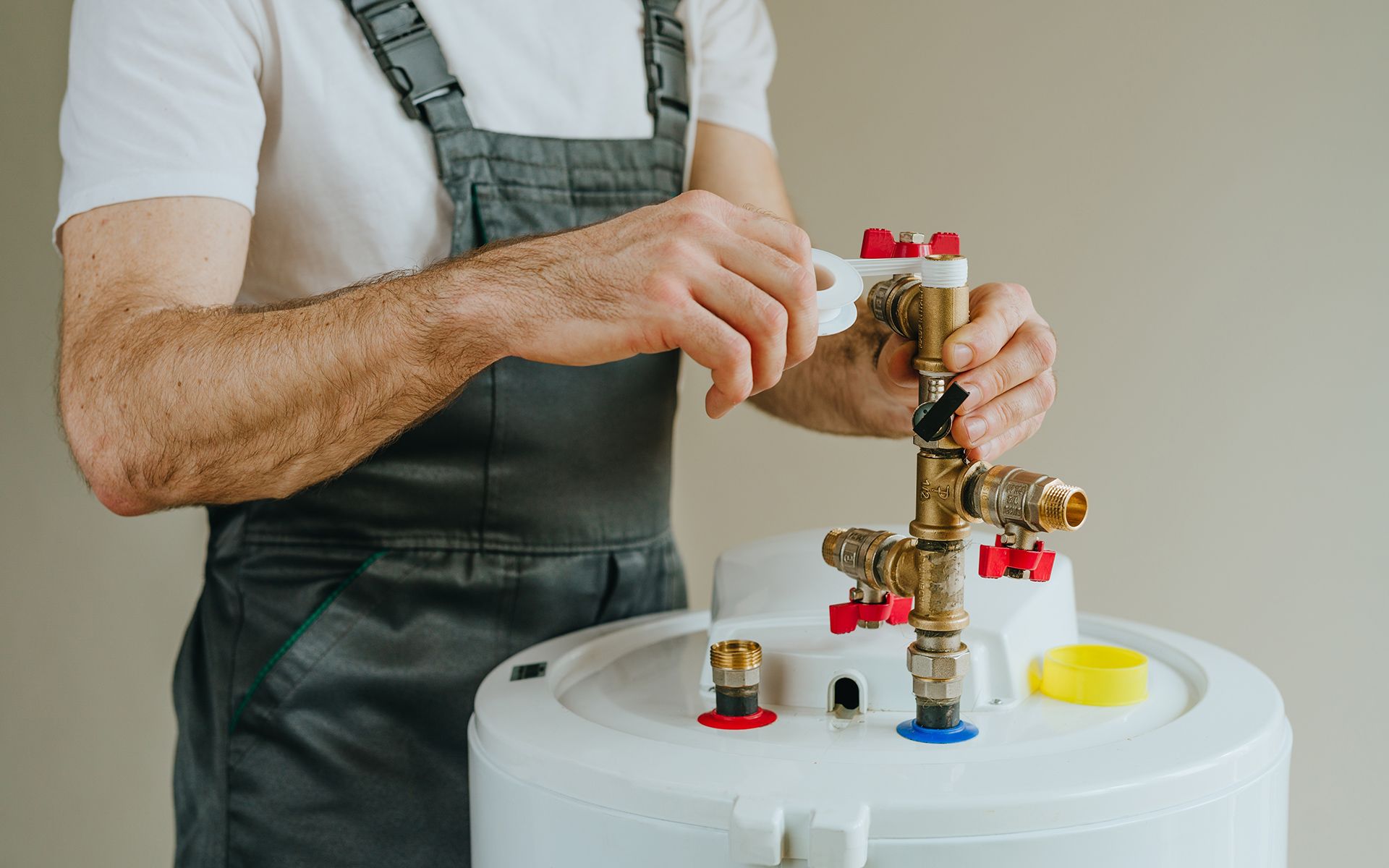 Plumber in overalls connecting pipes to a water heater.