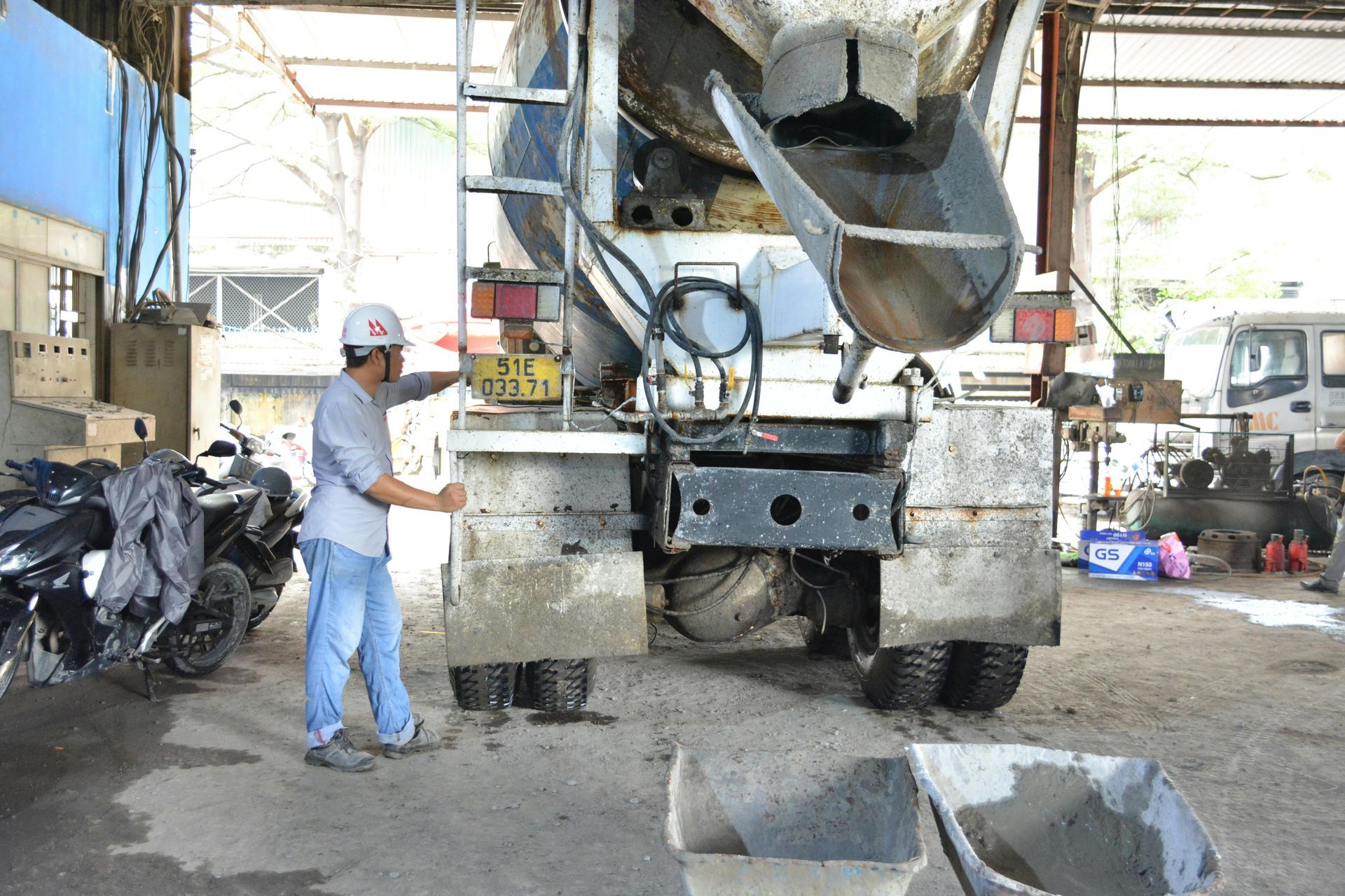 A man is standing next to a concrete mixer truck in a garage.
