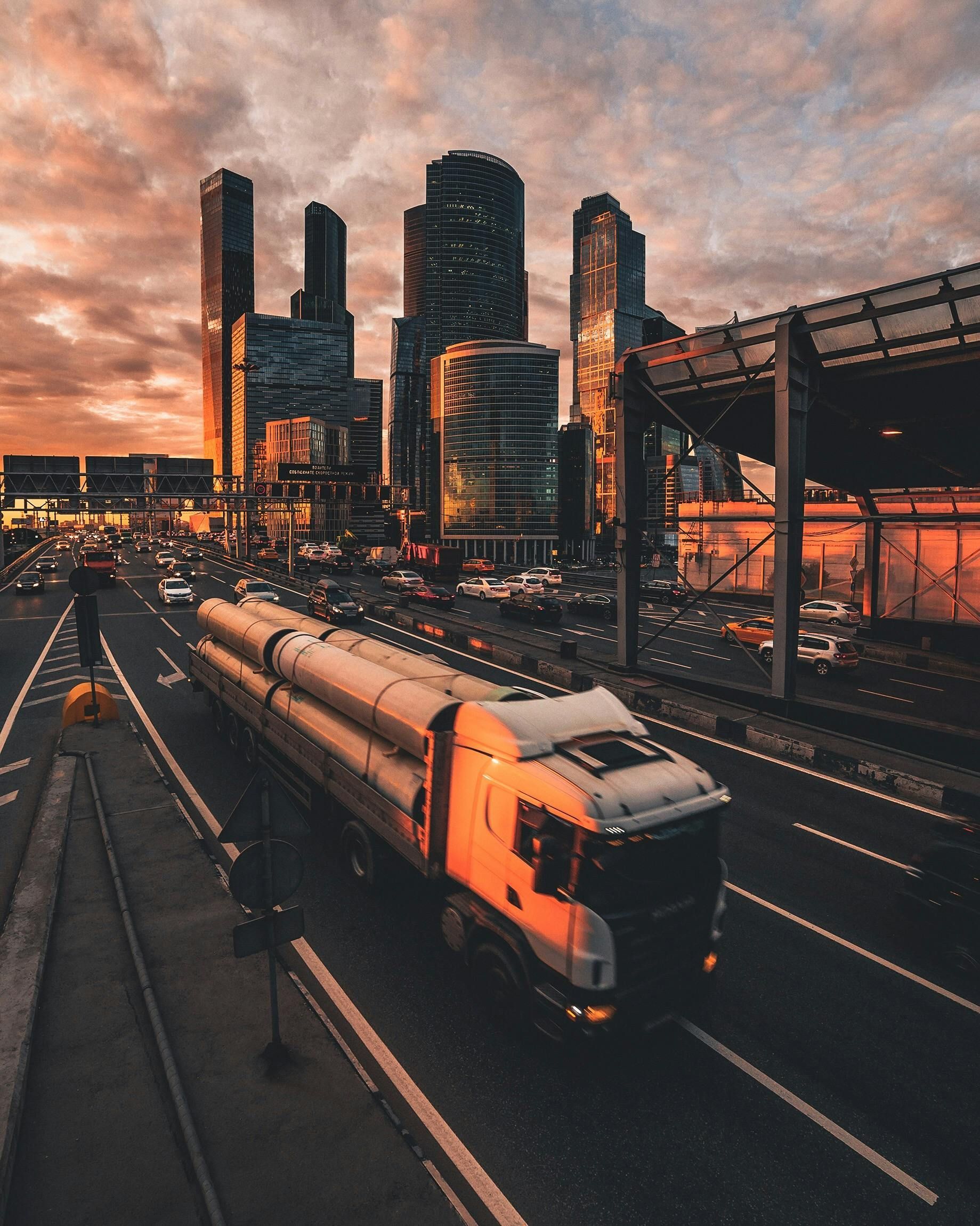 A truck is driving down a highway in front of a city skyline.