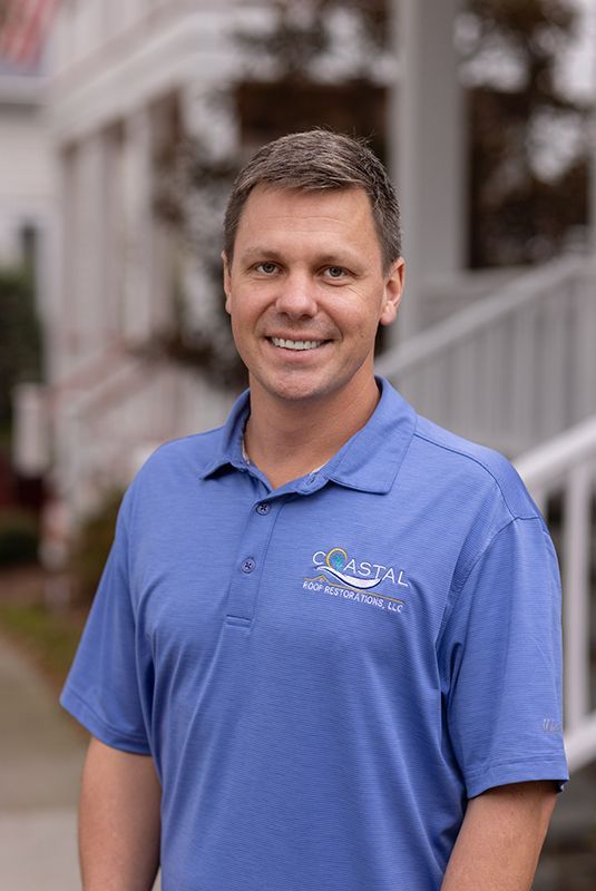 A man in a blue shirt is standing in front of a house.