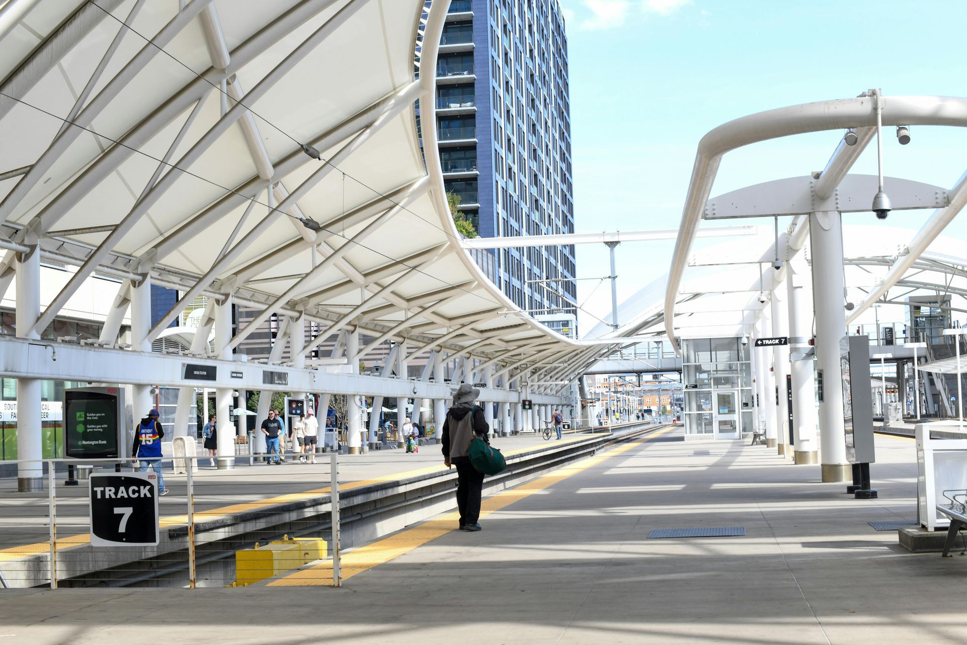 Airport walkway with covered platforms, a lone traveler, and a train platform sign reading 7