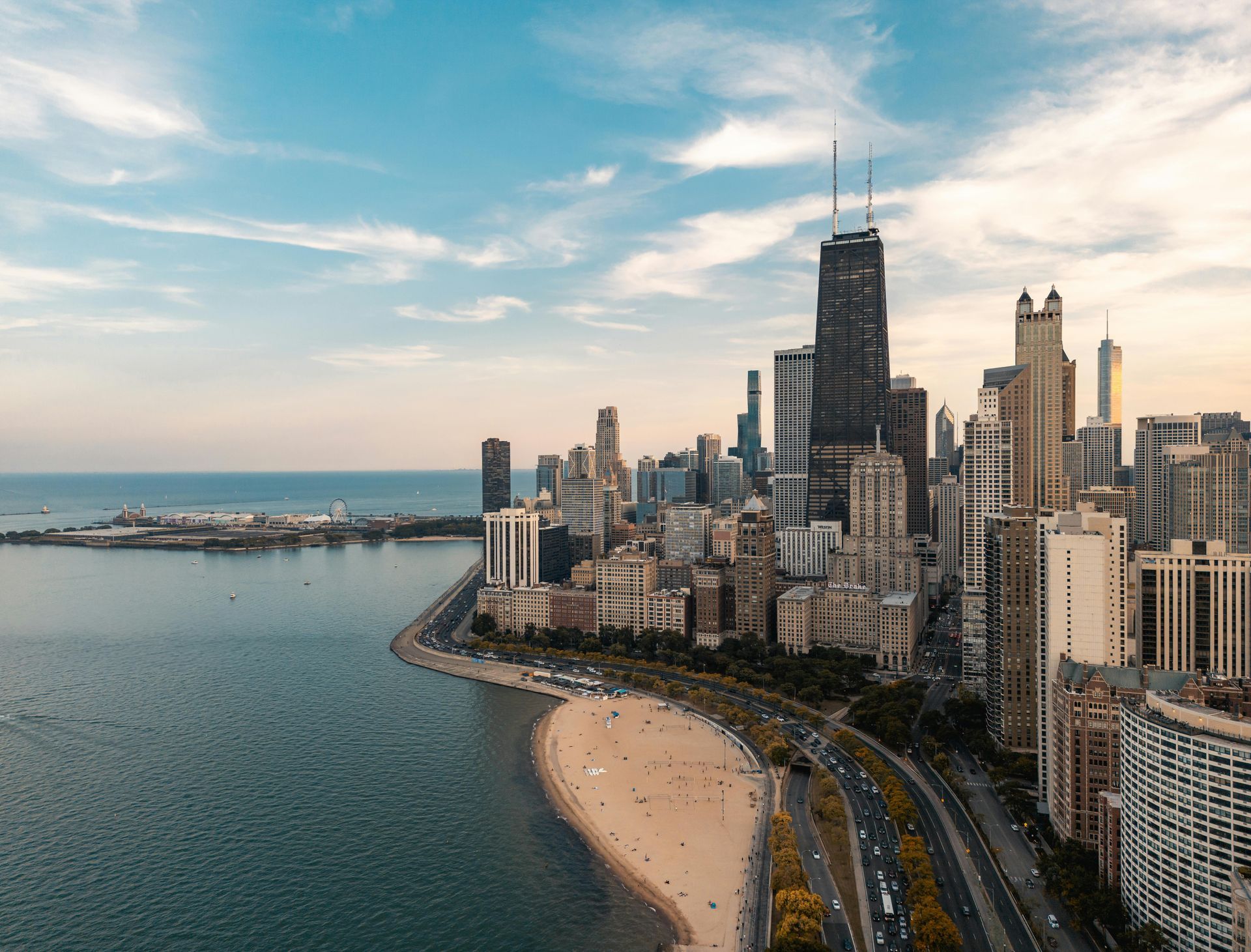 Aerial view of a lakeside city skyline with beach, waterfront road, and calm water at sunset