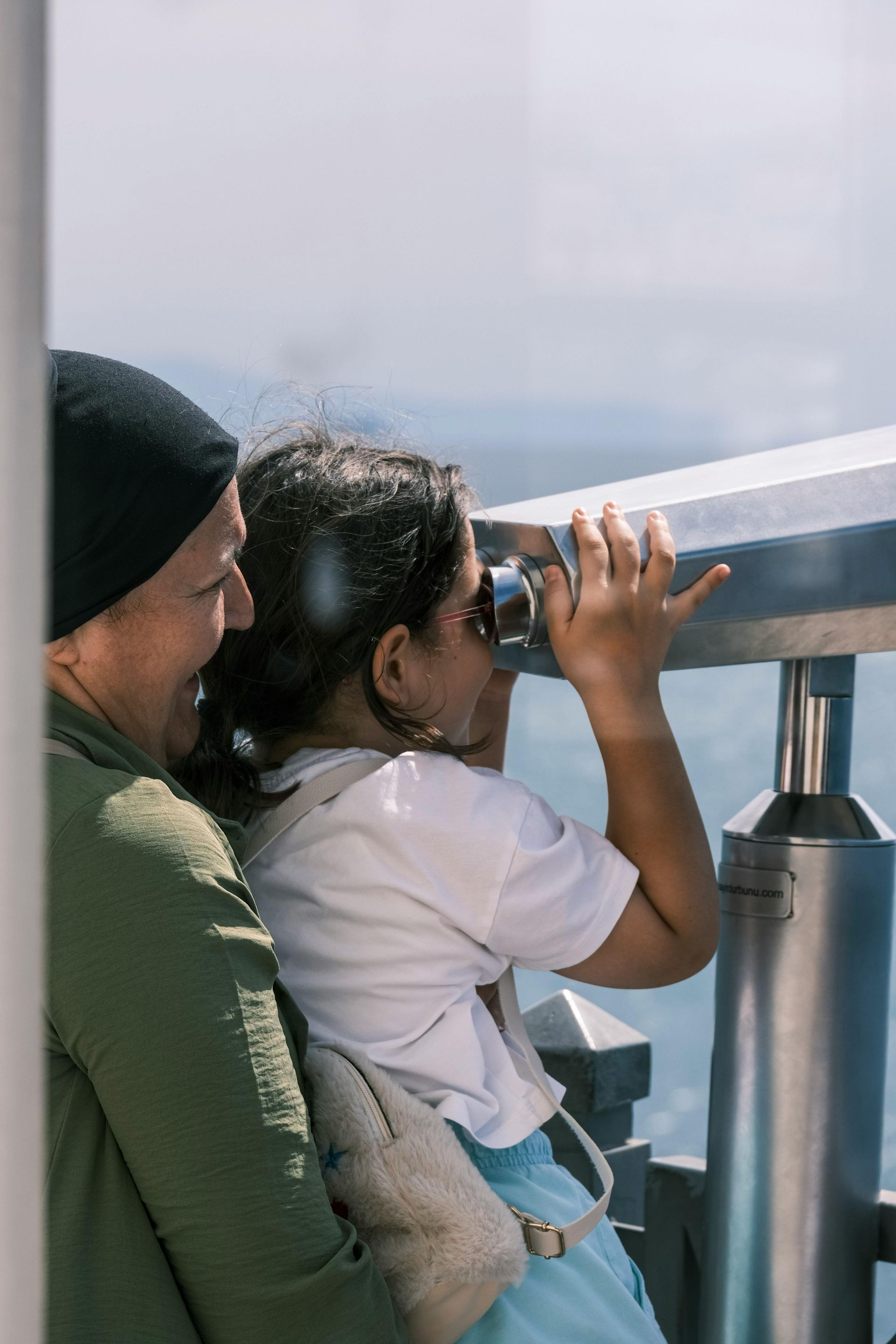 Two people look through a telescope on a seaside observation deck.
