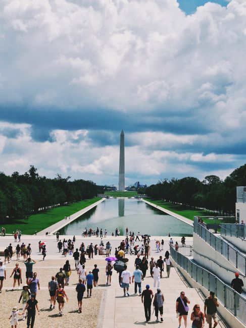 Crowd walking along the Reflecting Pool toward the Washington Monument under cloudy skies