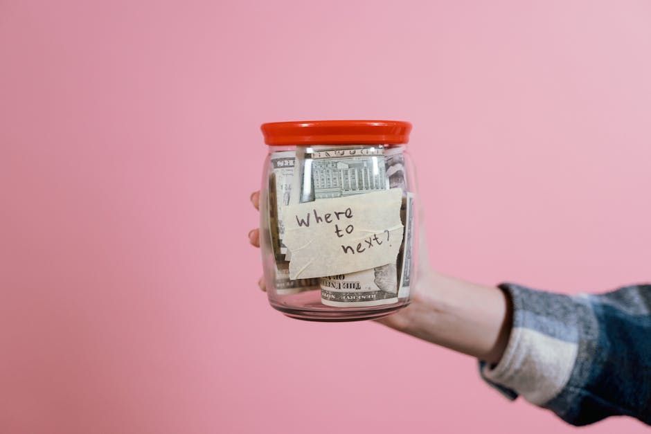 Hand holding a glass jar with a red lid labeled “wishes for new year” against a pink background