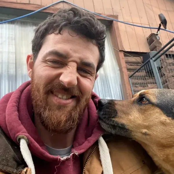 A man with a beard is smiling while holding a dog.