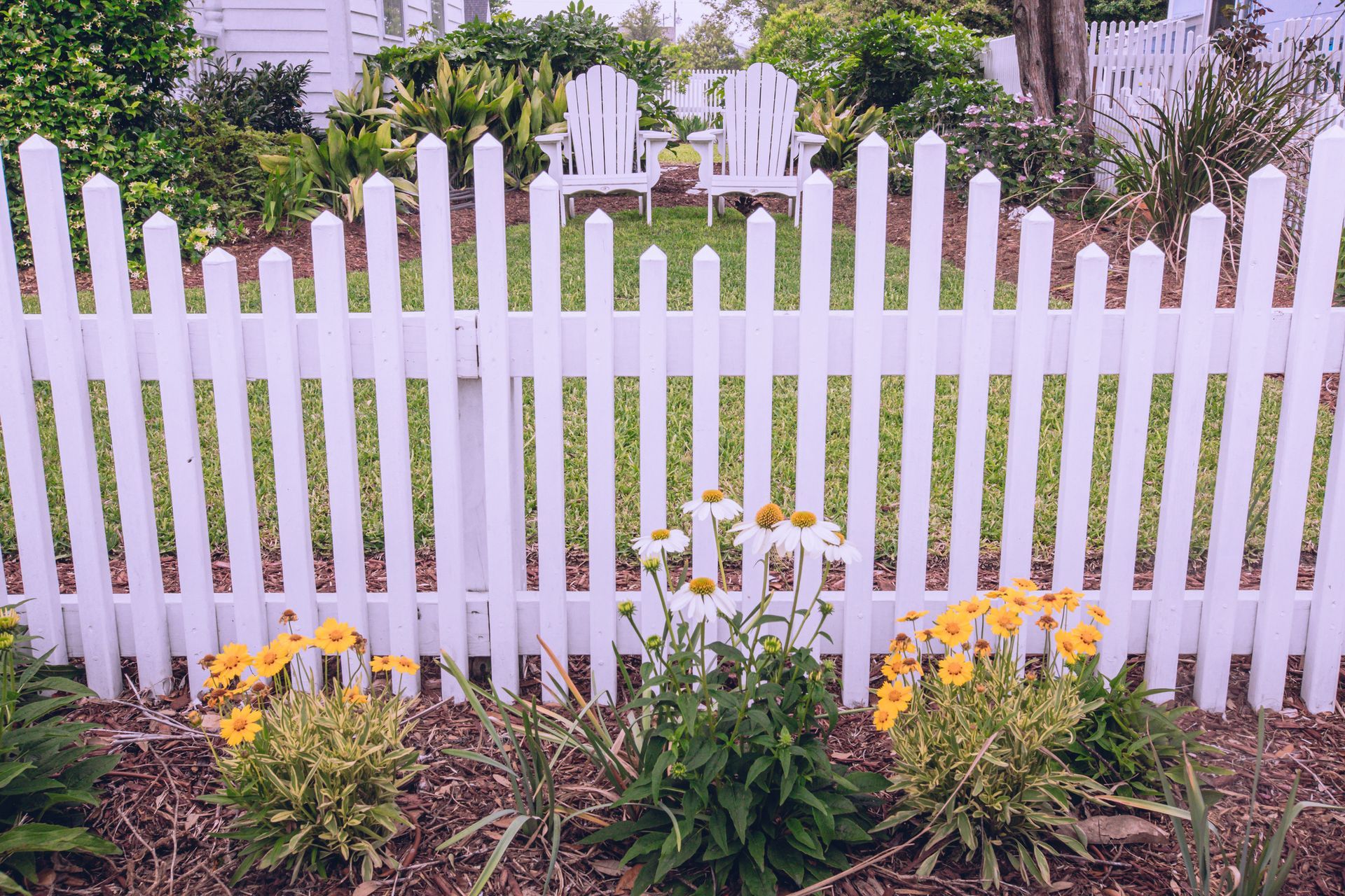 A white picket fence surrounds a garden with yellow flowers.