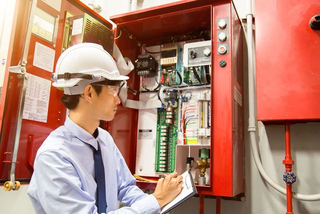 A man in a hard hat is looking at a fire alarm system.