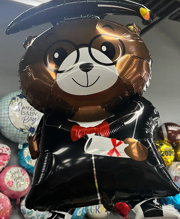 A black graduation bear balloon with glasses, cap, and red bow tie, holding a diploma-shaped gift.