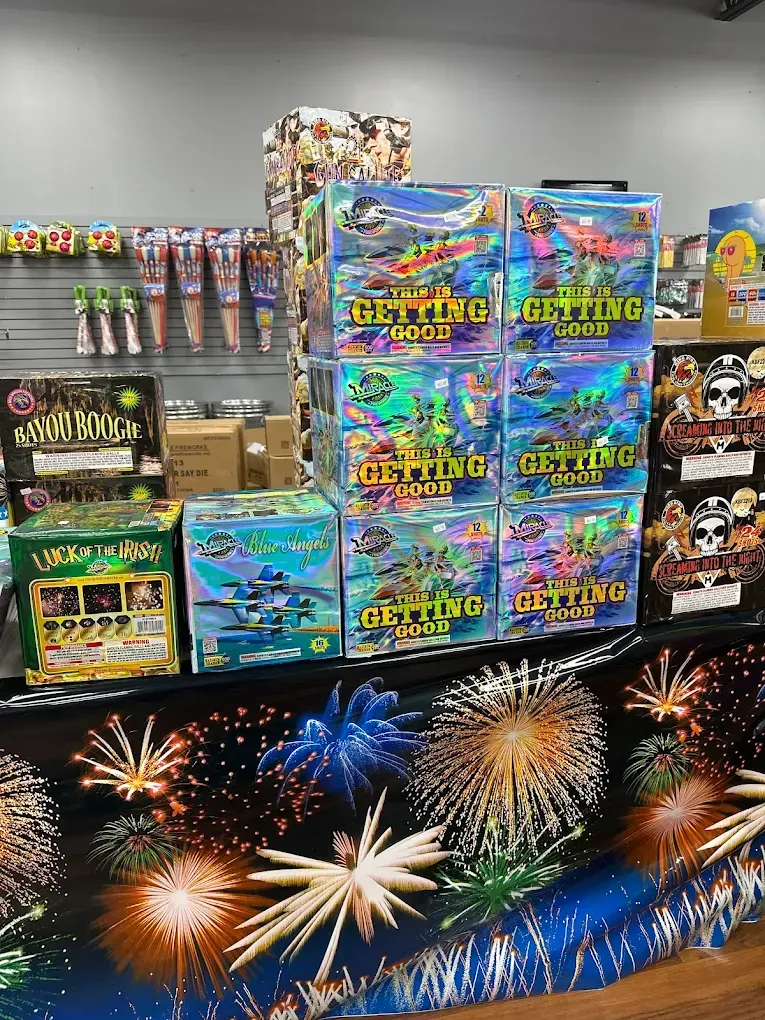 Fireworks display rack with colorful boxed fireworks and sparklers on shelves, plus burst graphics below