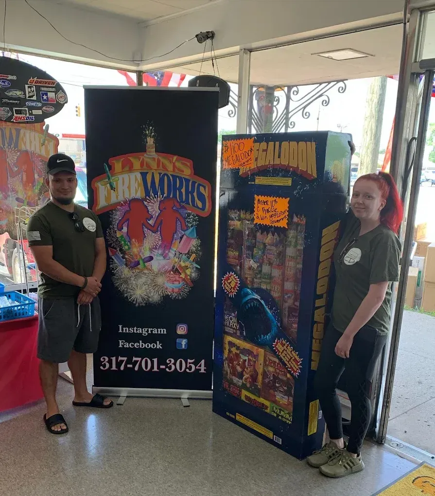 Two people stand beside colorful event banners in a booth, with tables and display items in the background.