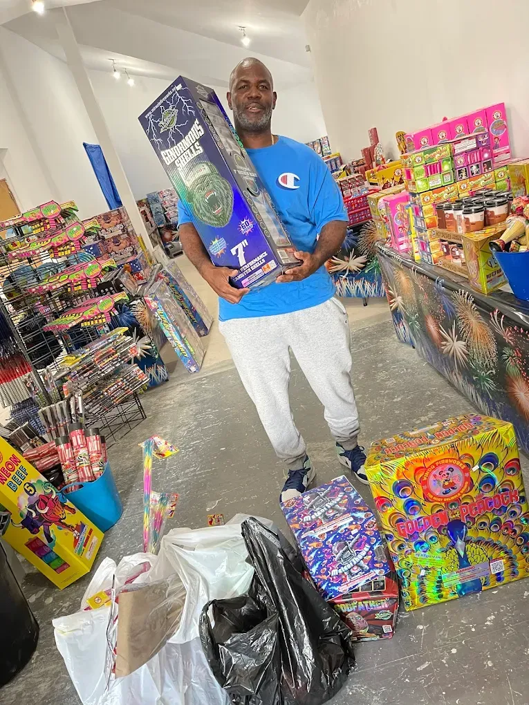 Man in a party store holding a blue gift bag, surrounded by colorful toys and party supplies.