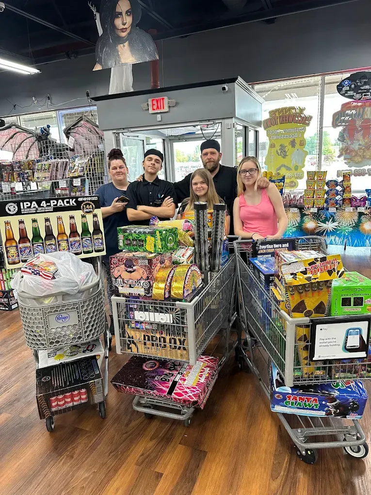 Store staff and volunteers posing with carts full of donated snack packs inside a convenience store.