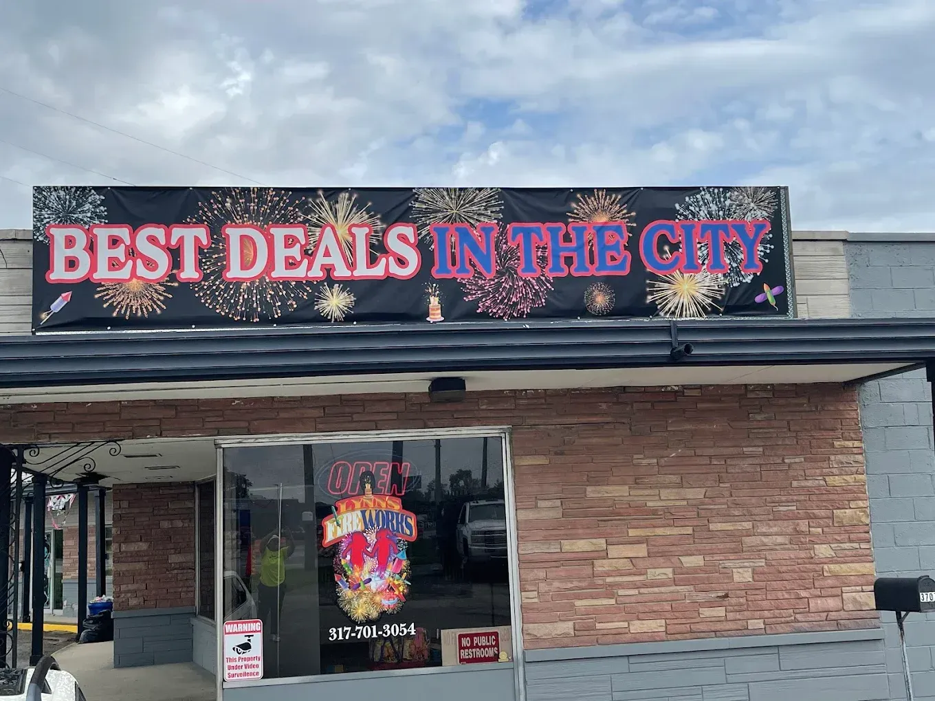 Storefront with large neon sign reading “BEST DEALS IN THE CITY” on a brick building