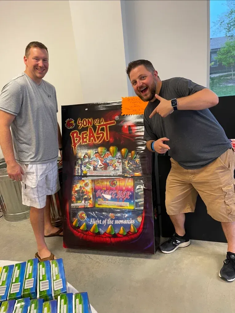Two men posing beside a colorful Beast arcade machine in a store, with stacked boxes in the foreground.