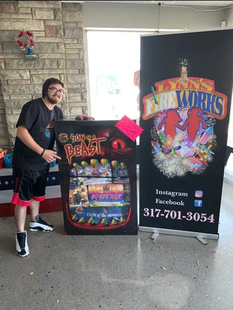 Man posing beside a colorful fireworks display sign and banner inside a lobby near a stone wall