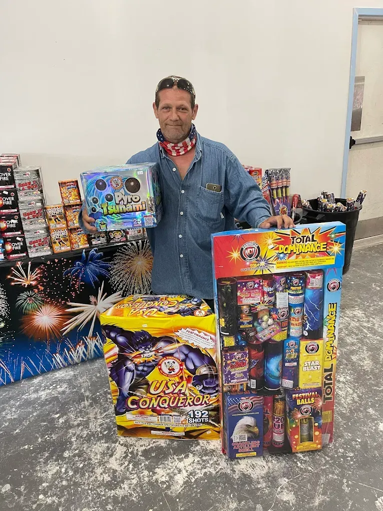 Man posing behind colorful fireworks boxes stacked in a shop-like setting