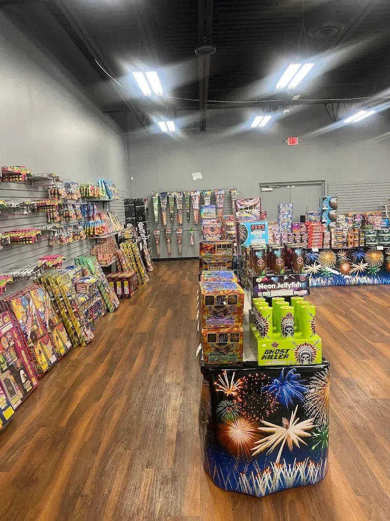 Fireworks store aisle with colorful pyrotechnics on shelves and display bins under bright ceiling lights