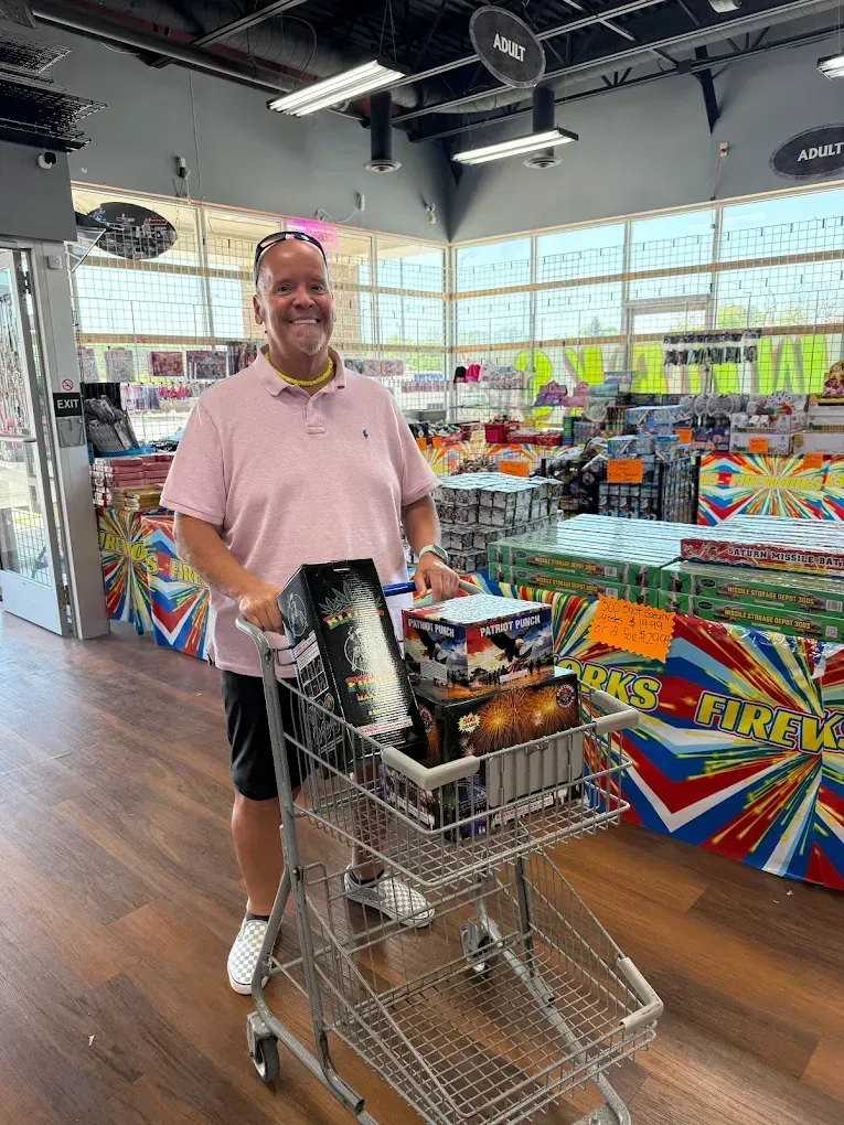 Person in pink shirt pushing a shopping cart in a brightly lit store with colorful checkout counters