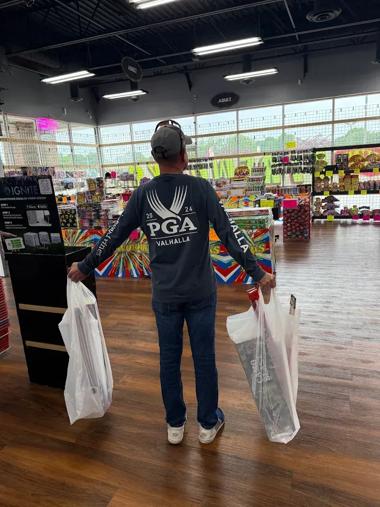 Person in a PGA jacket holding shopping bags in a brightly lit grocery store aisle.