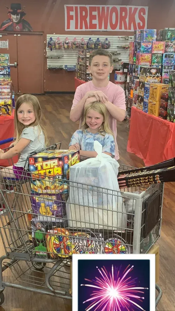 Three children with shopping carts full of fireworks in a fireworks store.