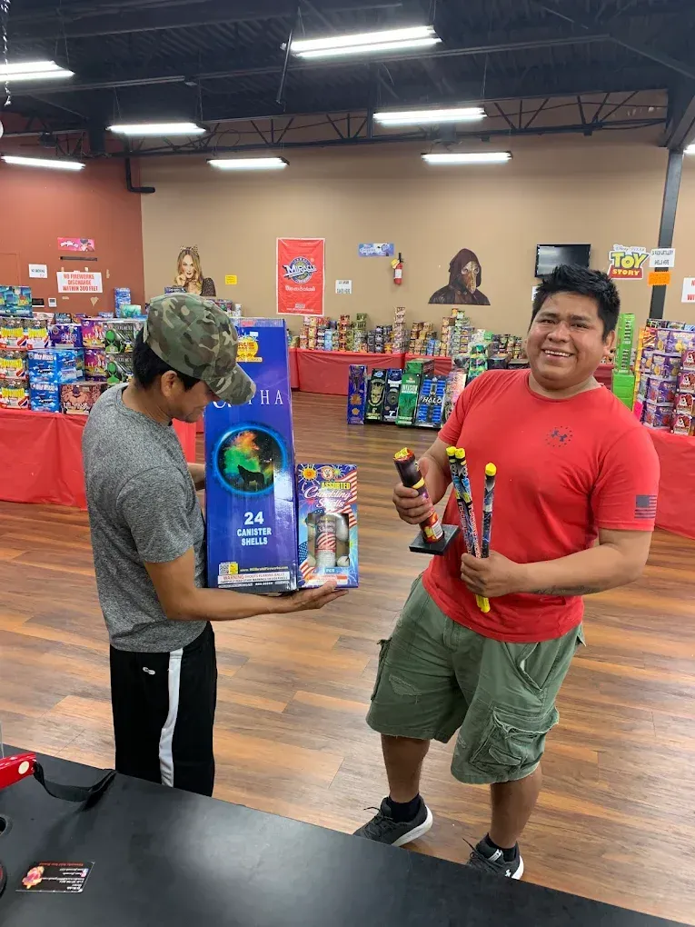 Two men in a store aisle, one holding a large blue toy box, the other smiling with an action figure.