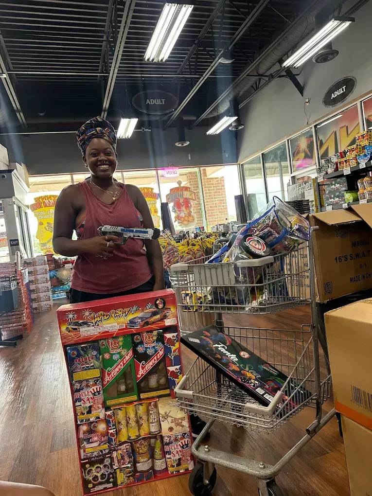 Woman smiling in a grocery store aisle beside a shopping cart filled with colorful snack boxes.