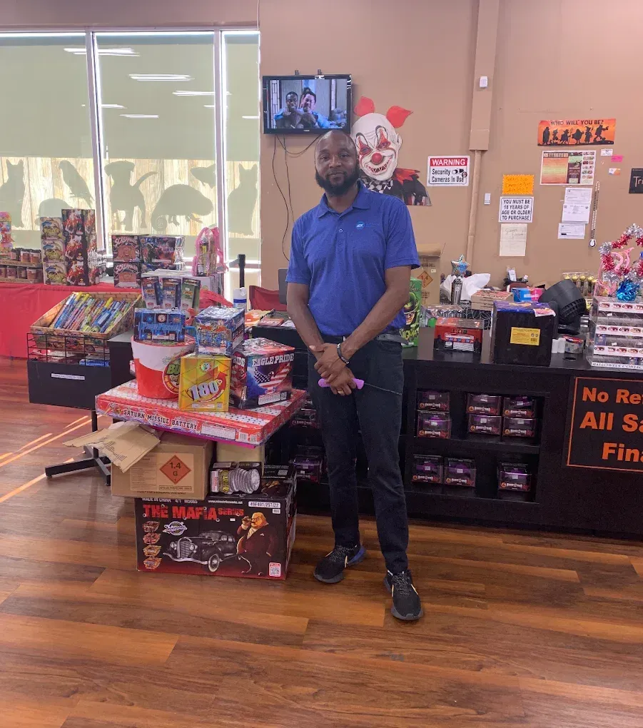 Man standing in a convenience store aisle beside a display of snacks and holiday decorations.