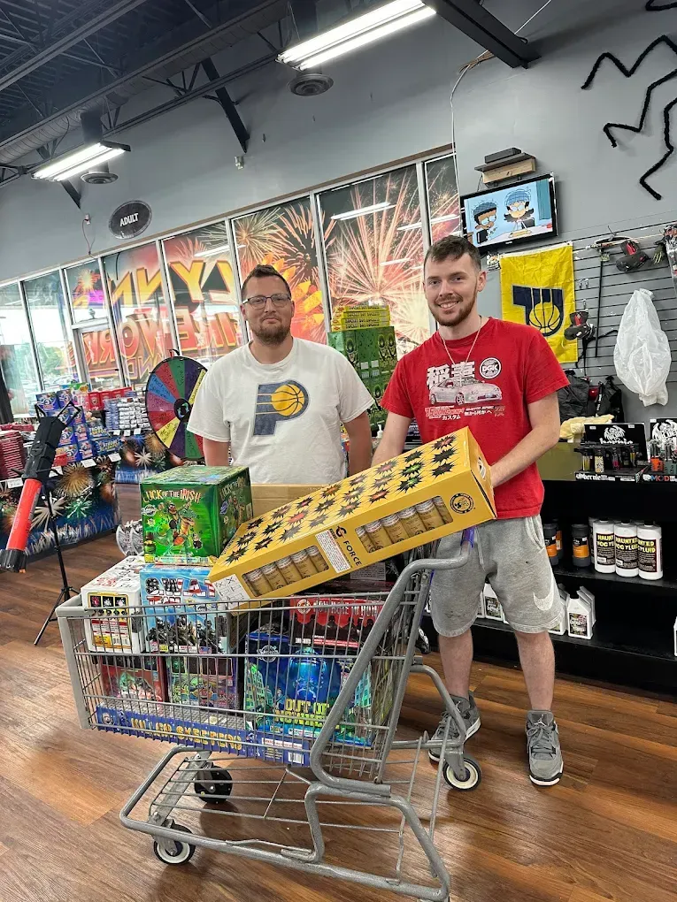 Two men standing behind a shopping cart full of toys in a colorful store aisle