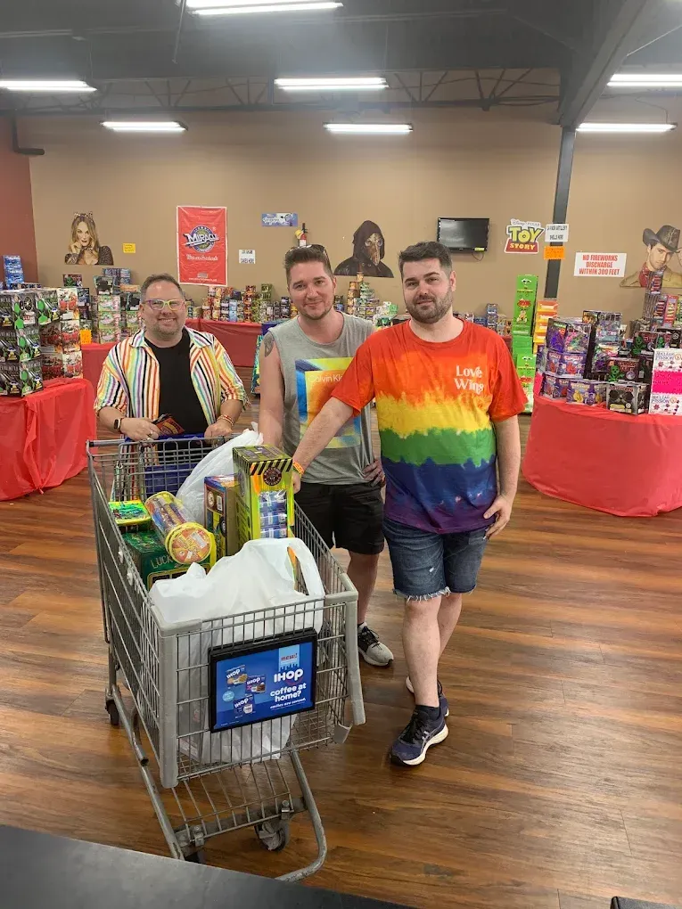 Three people posing with a shopping cart full of canned goods in a store or donation drive setting