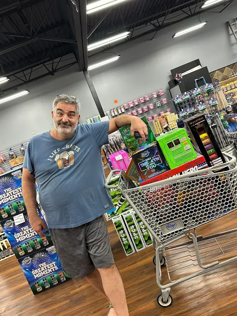 Man leaning on a shopping cart in a store aisle beside stacked colorful drinks and packaged goods