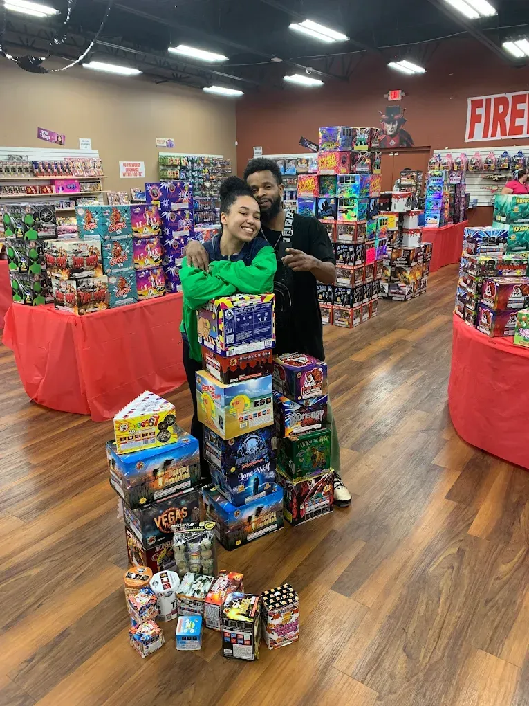 Two people posing behind a colorful stack of toy boxes in a store aisle at a toy drive display.