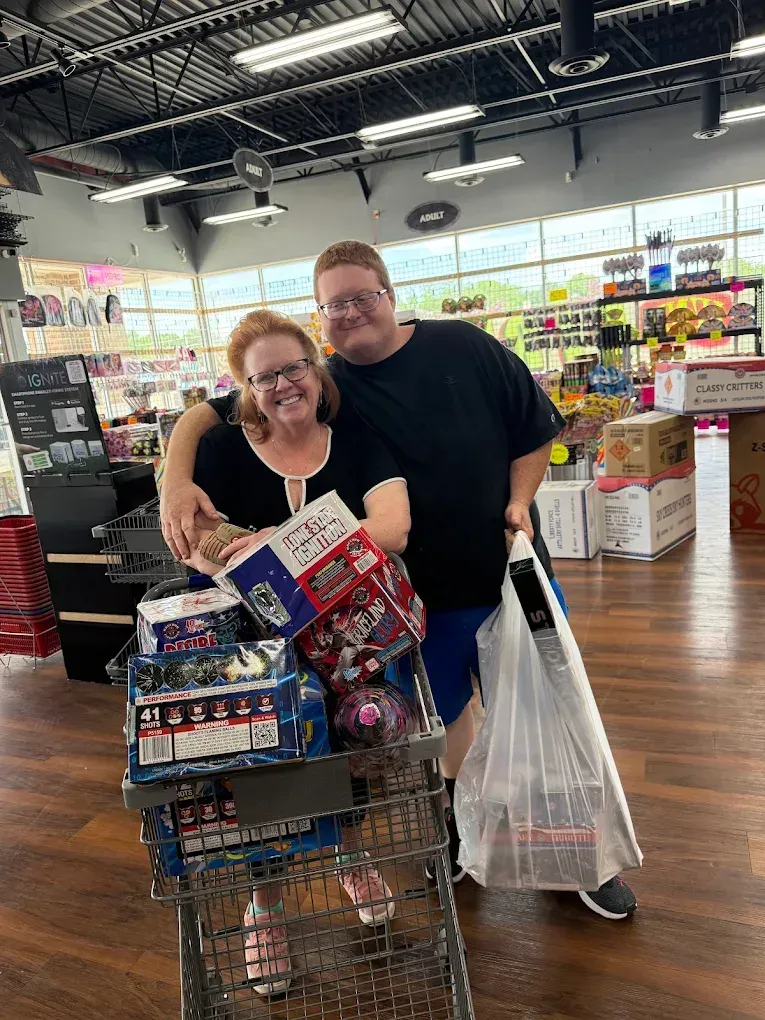 Two people smiling in a store aisle beside a shopping cart piled high with boxed items