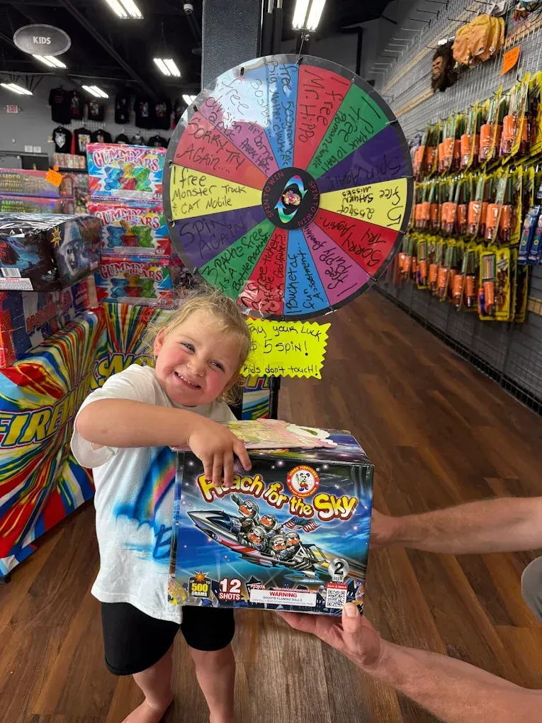 Child smiling in a candy store, holding a Pokémon box in front of a colorful prize wheel.