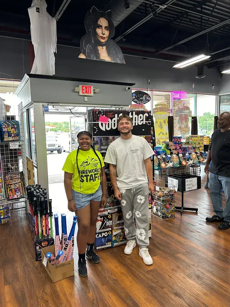 Two people posing in a souvenir shop with racks of merchandise and wood flooring