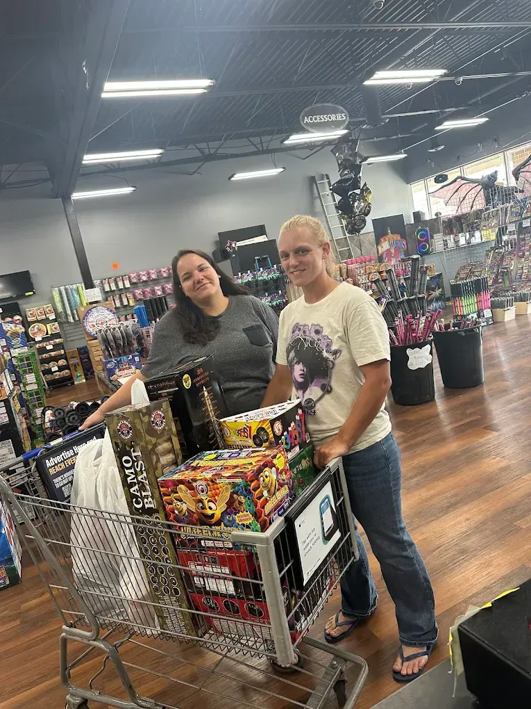 Two shoppers stand beside a cart full of colorful snacks in a store aisle.