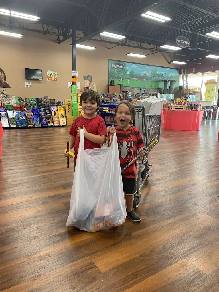 Two children smiling and holding a large white shopping bag in a store aisle.