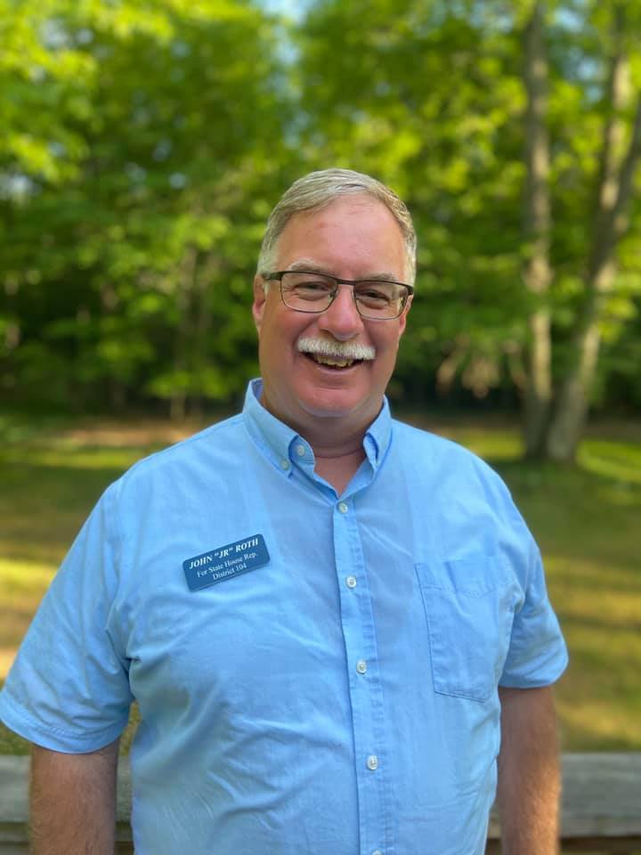 A man wearing glasses and a blue shirt is smiling for the camera.