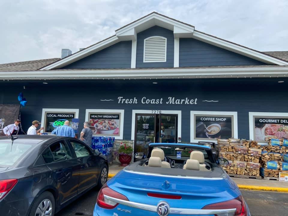 A blue car is parked in front of a fresh coast market.