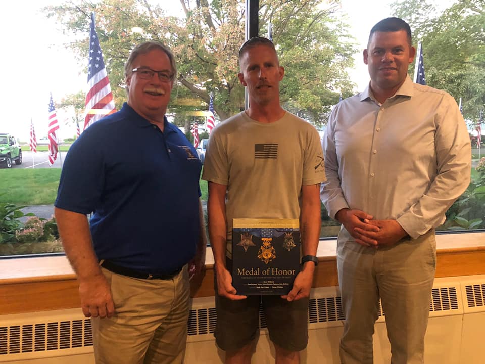 Three men are standing next to each other holding a book.