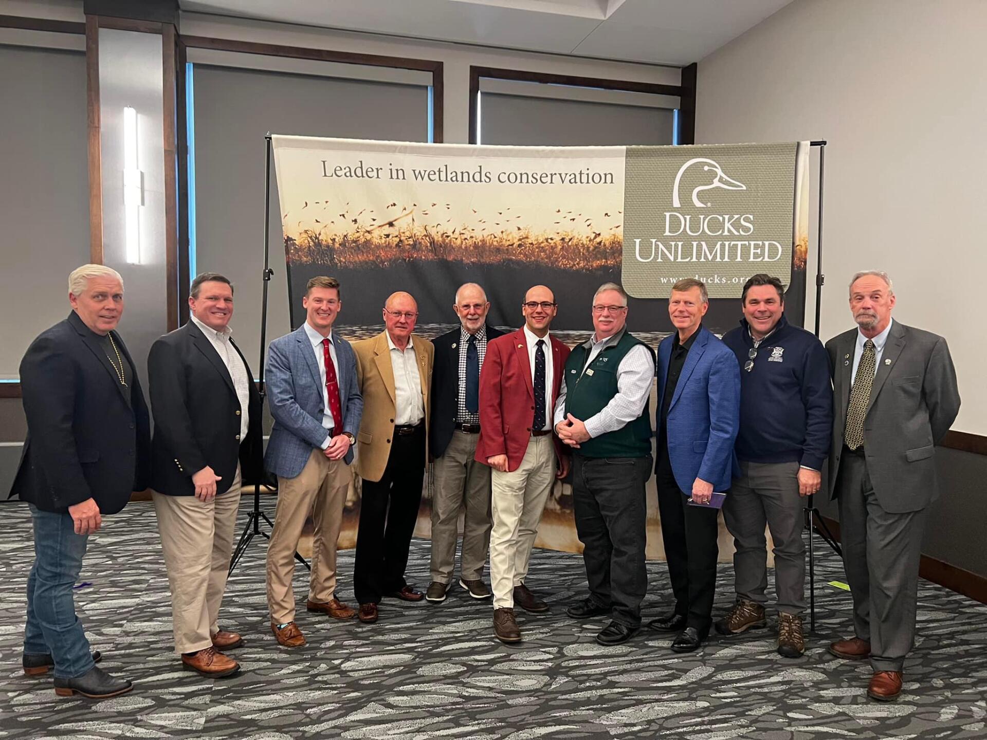 A group of men are posing for a picture in front of a ducks unlimited banner.