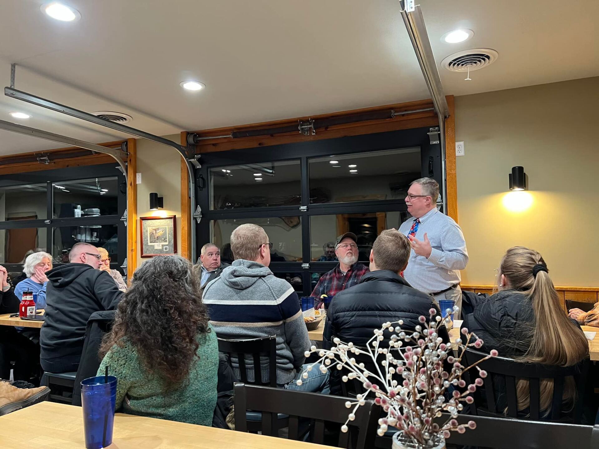 A man is giving a presentation to a group of people sitting at tables in a restaurant.