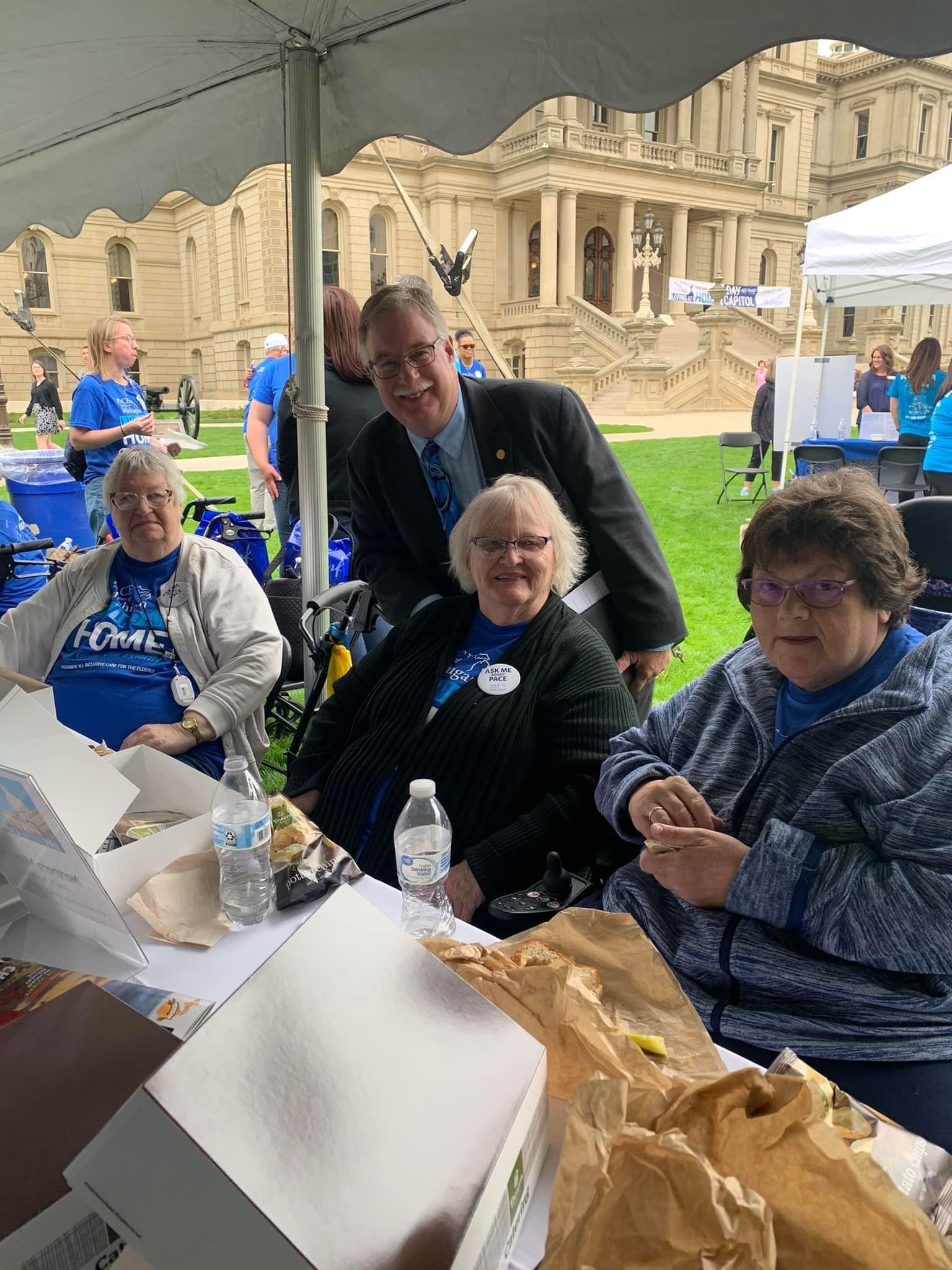 A group of people are sitting under a tent in front of a building.
