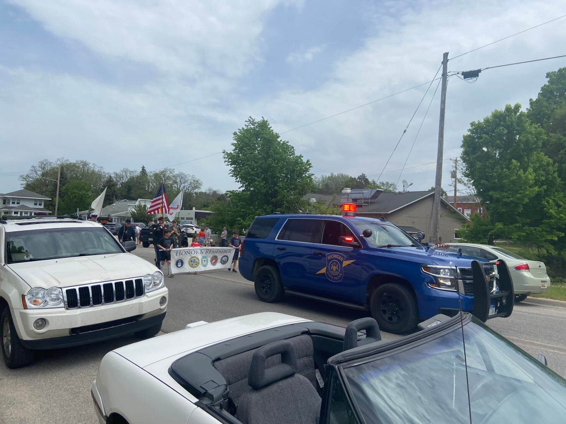 A blue police car is driving down a street next to a white convertible.