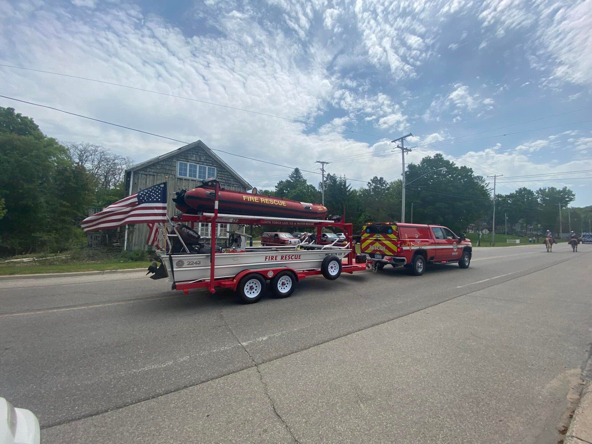 A red truck is pulling a boat on a trailer down a street.